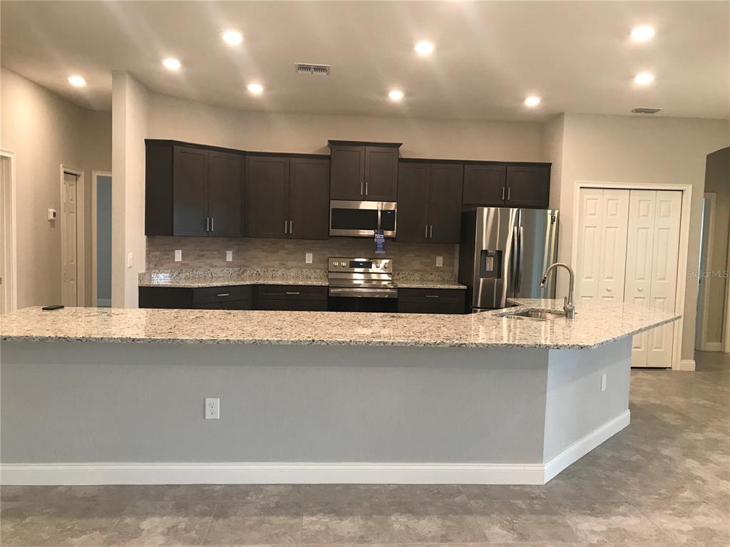 A kitchen features dark wood cabinets, granite countertops, stainless steel appliances, and a breakfast bar — 1437 CYPRESS VIEW LANE, LAKELAND, FL