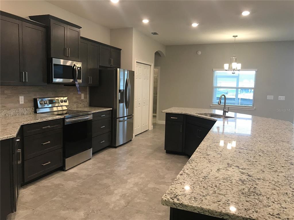 A kitchen features dark cabinets, granite countertops, stainless steel appliances, and light tile flooring — 1437 CYPRESS VIEW LANE, LAKELAND, FL