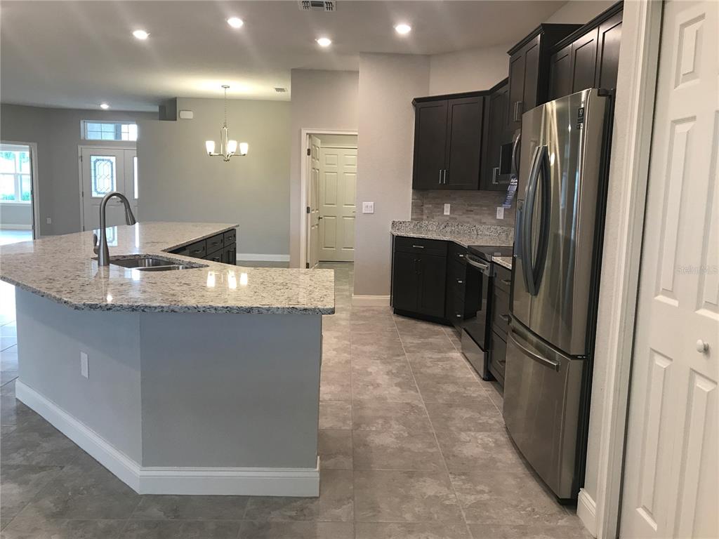 A kitchen features dark cabinets, granite countertops, stainless steel appliances, and gray tile flooring — 1437 CYPRESS VIEW LANE, LAKELAND, FL