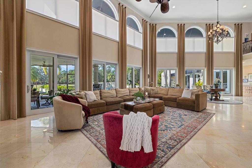 A spacious living room features high ceilings, large arched windows, tile floors, and a sectional sofa — 3550 SARASOTA GOLF CLUB BOULEVARD, SARASOTA, FL