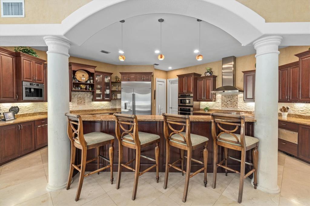 A kitchen features a curved island with four wooden bar stools under an arched ceiling — 3550 SARASOTA GOLF CLUB BOULEVARD, SARASOTA, FL