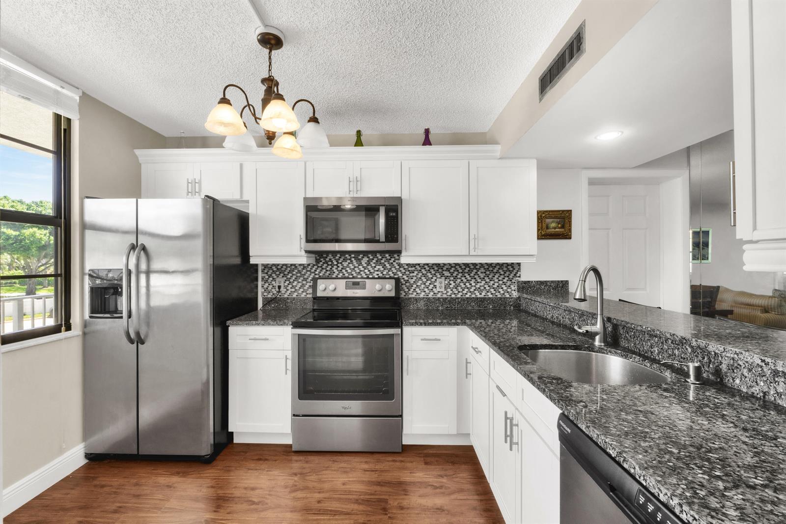 A kitchen features white cabinets, stainless steel appliances, granite countertops, and wood-look flooring — 3716 Whitehall Drive # 202, West Palm Beach FL 33401, WEST PALM BEACH, FL