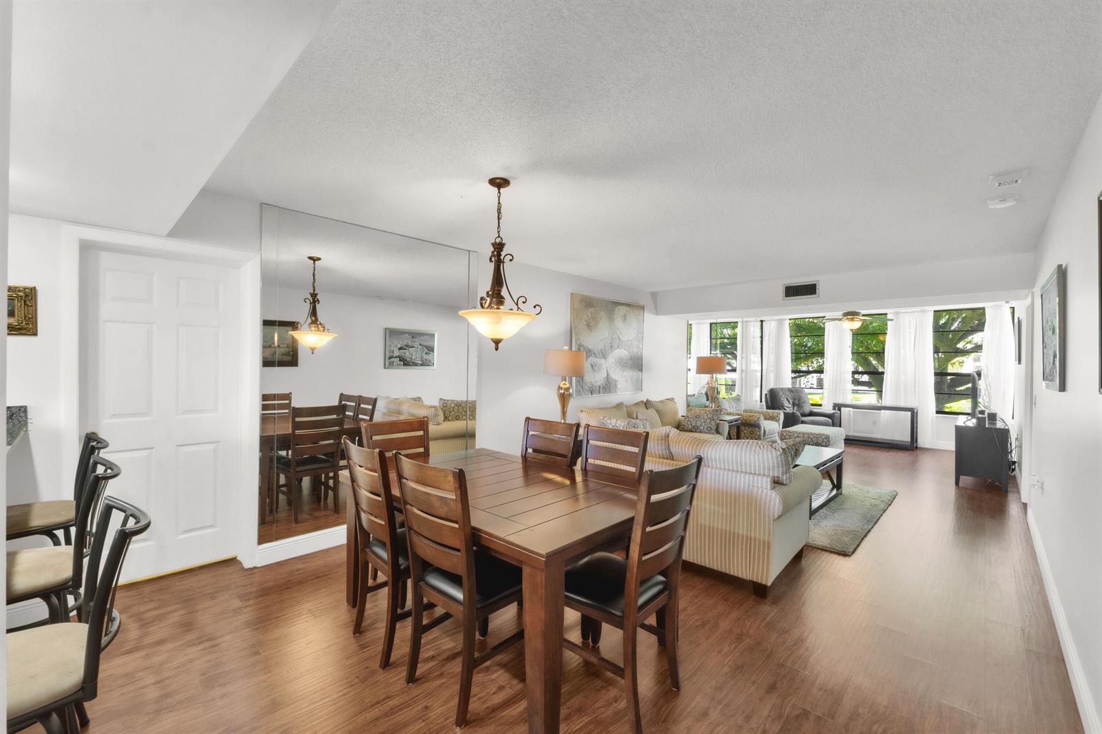 A dining area with a wooden table and chairs sits adjacent to a living room — 3716 Whitehall Drive # 202, West Palm Beach FL 33401, WEST PALM BEACH, FL