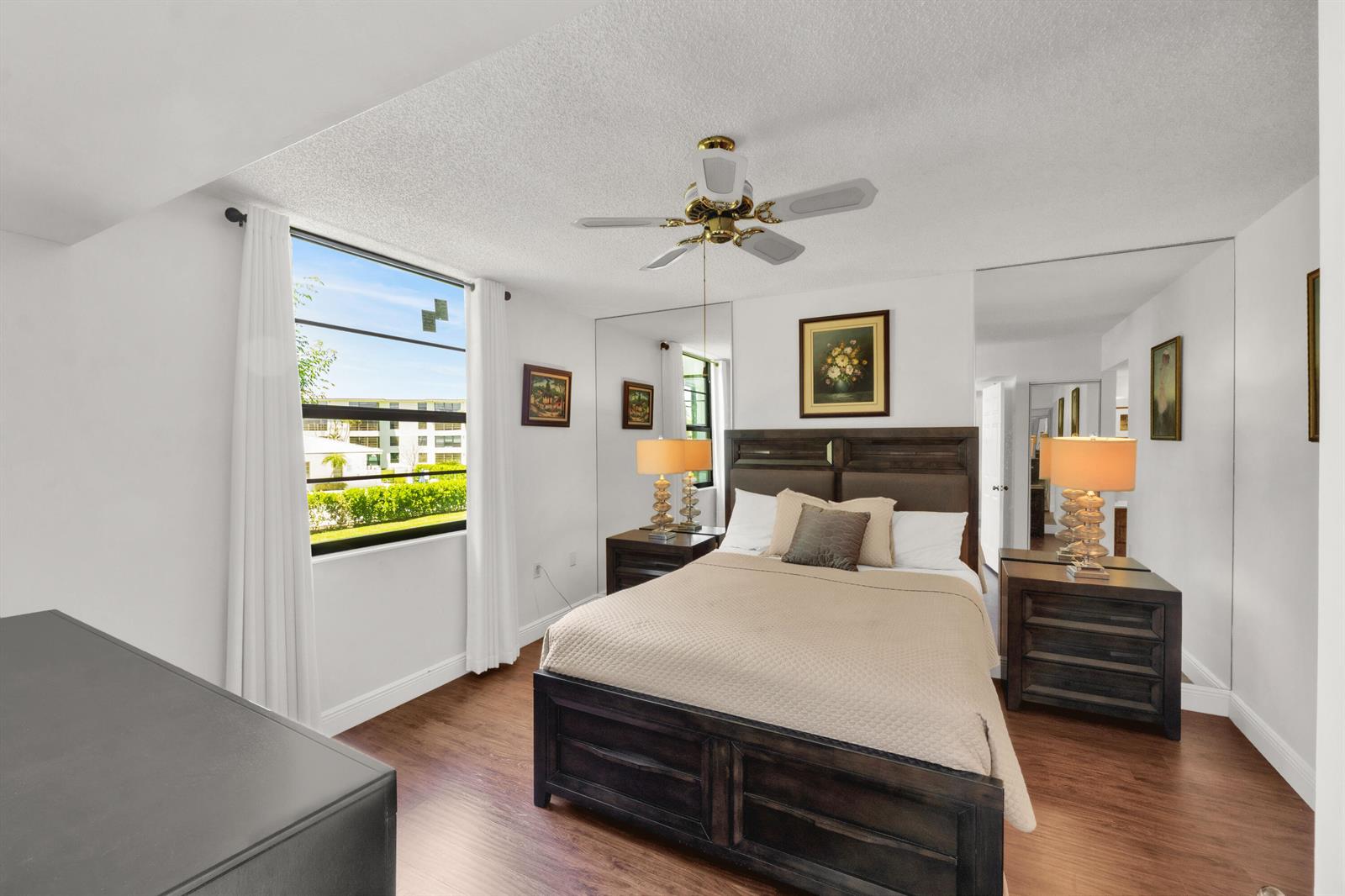 A bedroom features a dark wood bed frame, mirrored closet doors, and wood-look flooring — 3716 Whitehall Drive # 202, West Palm Beach FL 33401, WEST PALM BEACH, FL