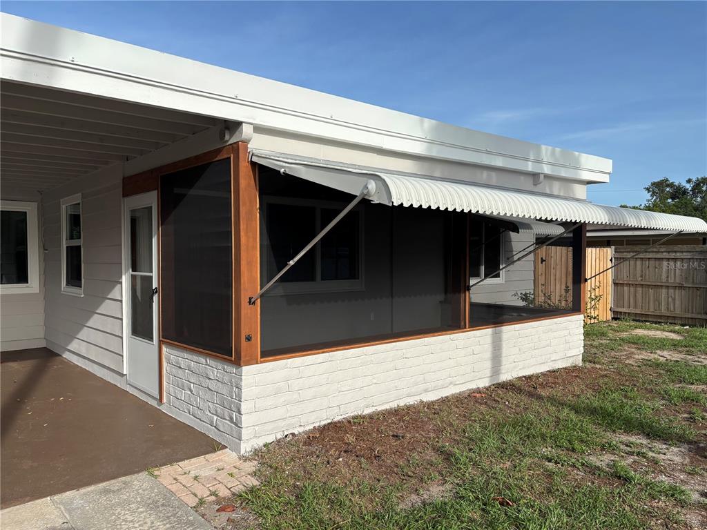 A screened-in porch with a white brick base and a metal awning sits outdoors — 5165 104TH WAY N, ST PETERSBURG, FL