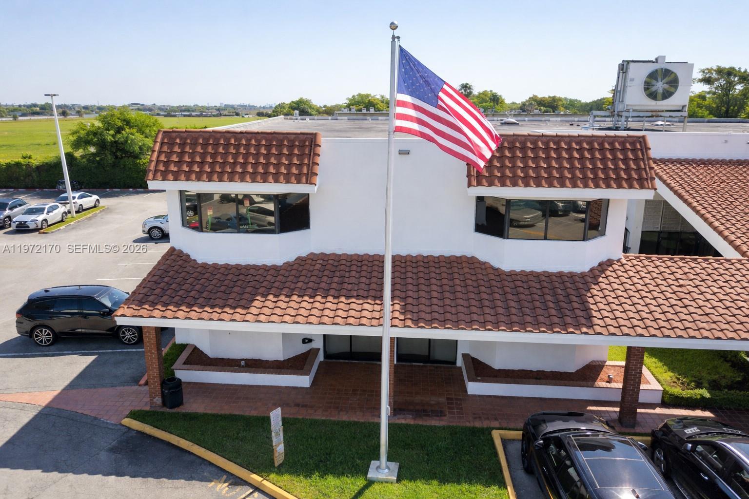 An exterior view of a two-story commercial building with a tiled roof and flagpole — 5969 NW 151st St, Miami Lakes FL 33014, MIAMI LAKES, FL