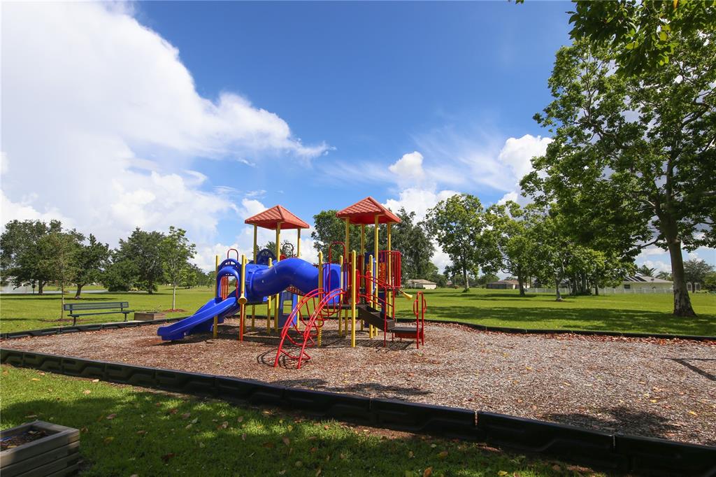A colorful playground structure sits on a wood-chipped surface in a grassy park area — 16085 CORUNA COURT, PUNTA GORDA, FL