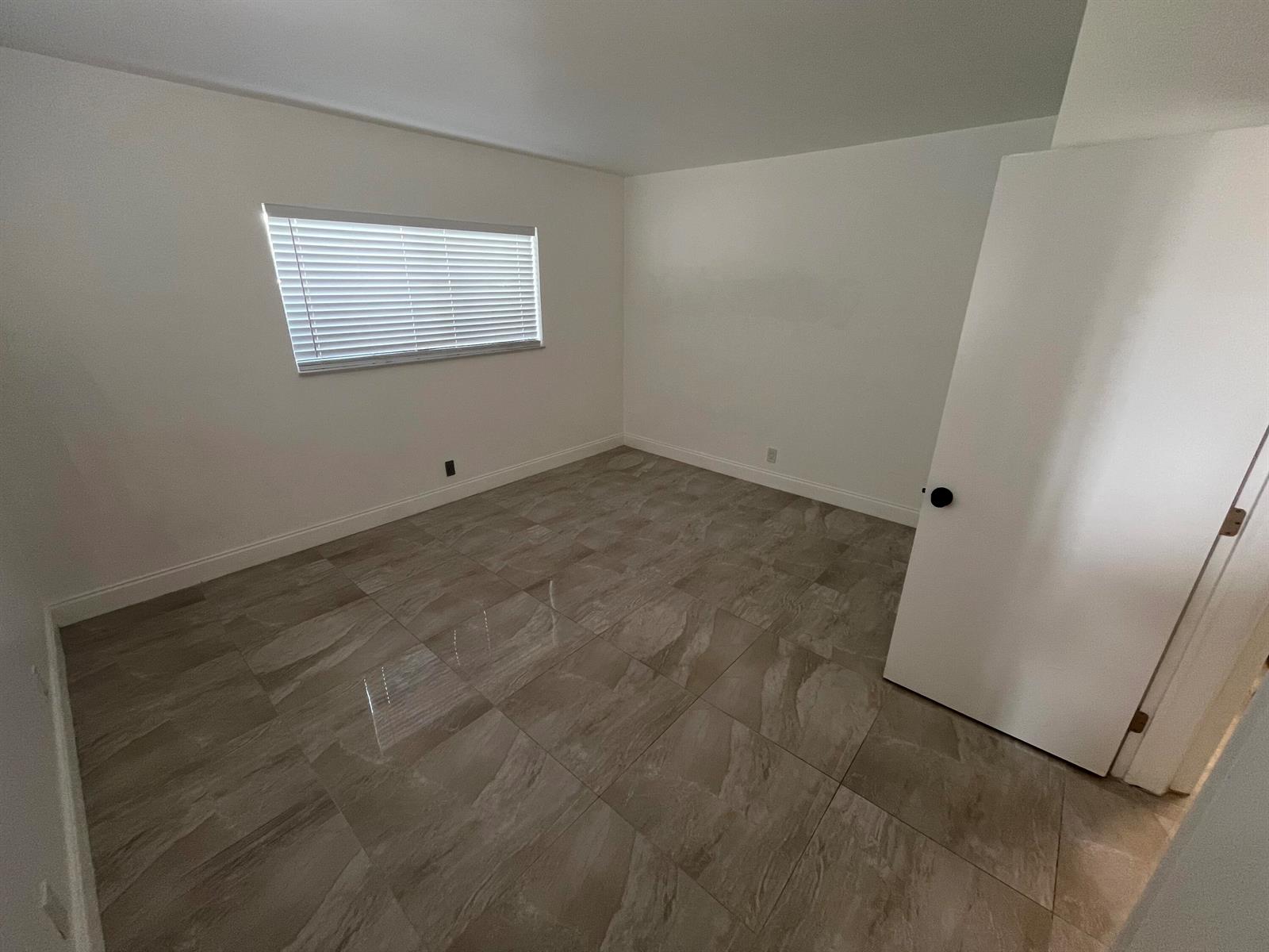 An empty bedroom features white walls, a single window with blinds, and large tiled flooring — 1019 SE 3rd Street # 3, Deerfield Beach FL 33441, DEERFIELD BEACH, FL
