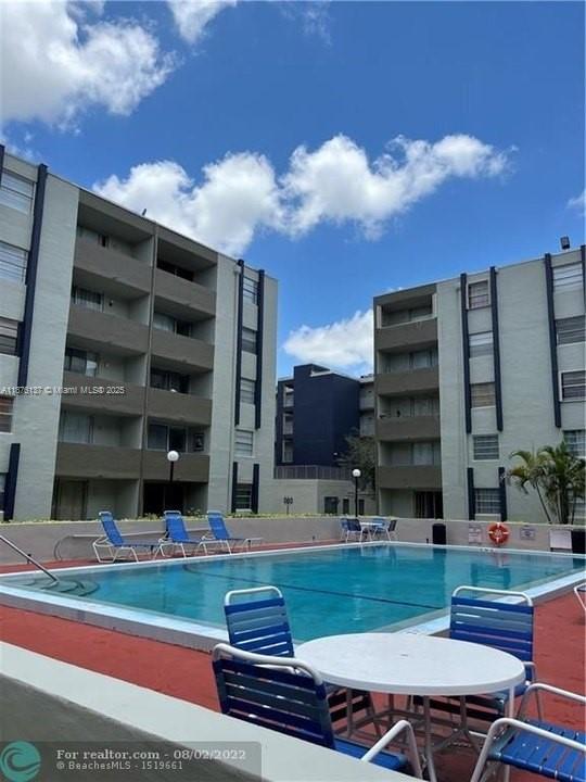 A swimming pool sits between two multi-story apartment buildings under a blue sky — 10000 NW 80th Ct # 2261, Hialeah Gardens FL 33016, HIALEAH GARDENS, FL