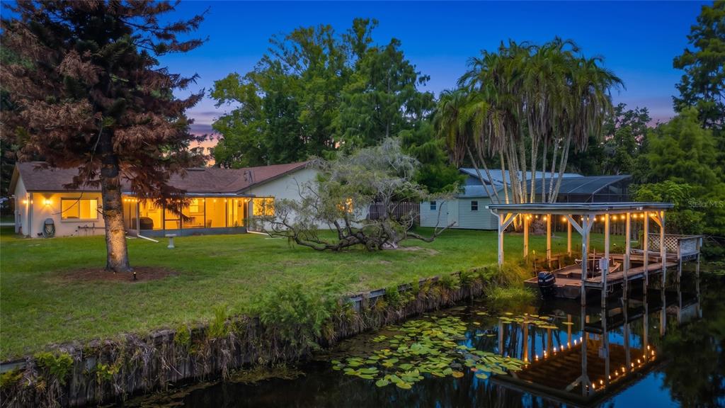 A house with a lawn and boat dock sits beside a canal at dusk — 28800 TAMMI DRIVE, TAVARES, FL