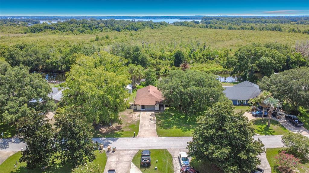An aerial view shows a single-story house with a brown roof surrounded by trees and water — 28800 TAMMI DRIVE, TAVARES, FL