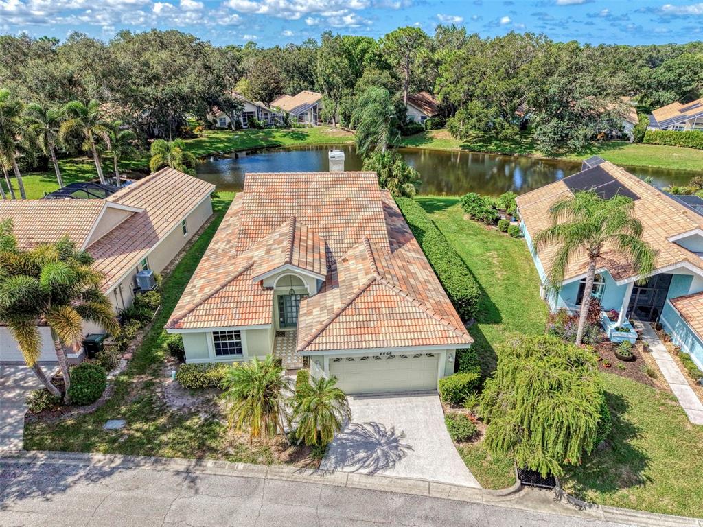 An aerial view of a single-story house with a tiled roof, driveway, and backyard pond — 4468 ASCOT CIRCLE N, SARASOTA, FL