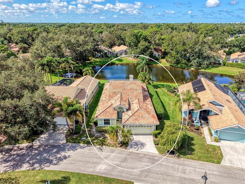 An aerial view shows a single-story house with a tiled roof situated by a pond — 4468 ASCOT CIRCLE N, SARASOTA, FL