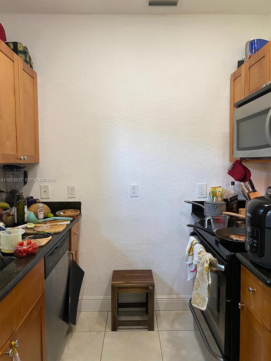 A kitchen features stainless steel appliances, wood cabinets, black countertops, and light-colored tile flooring — 851 80th St, Miami Beach FL 33141, MIAMI BEACH, FL