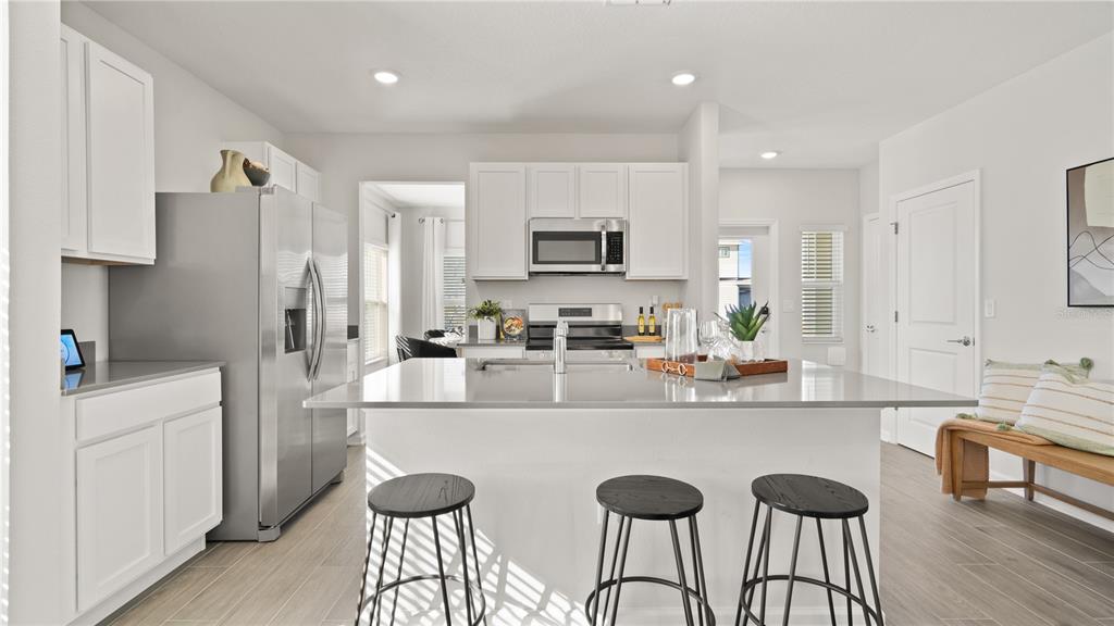 A modern kitchen features white cabinetry, stainless steel appliances, a large island, and bar stools — 4378 BENTGRASS BEND, ST CLOUD, FL