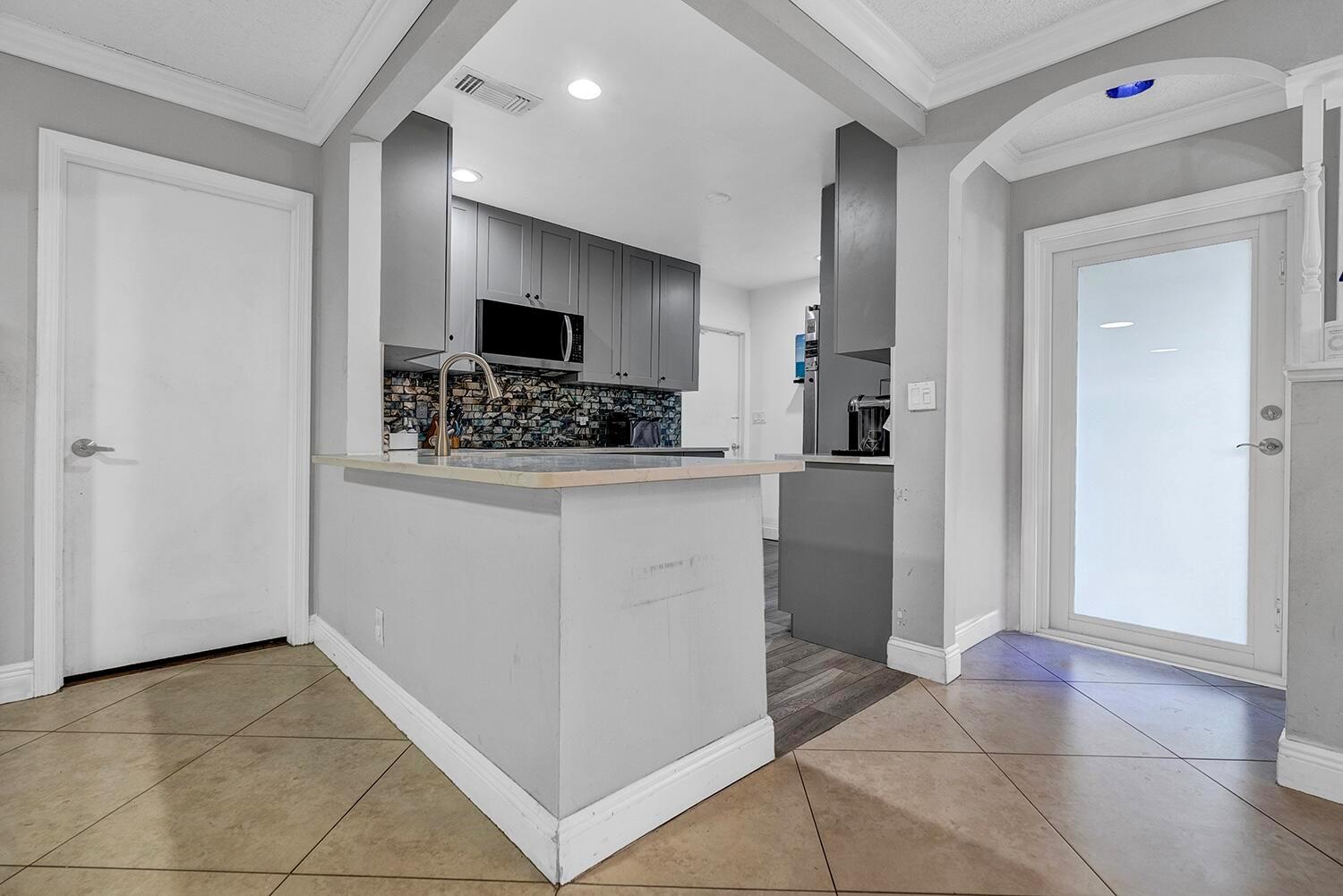 A kitchen with gray cabinets, a tiled backsplash, and a breakfast bar overlooks a tiled floor — 9544 Richmond Circle, Boca Raton FL 33434, BOCA RATON, FL