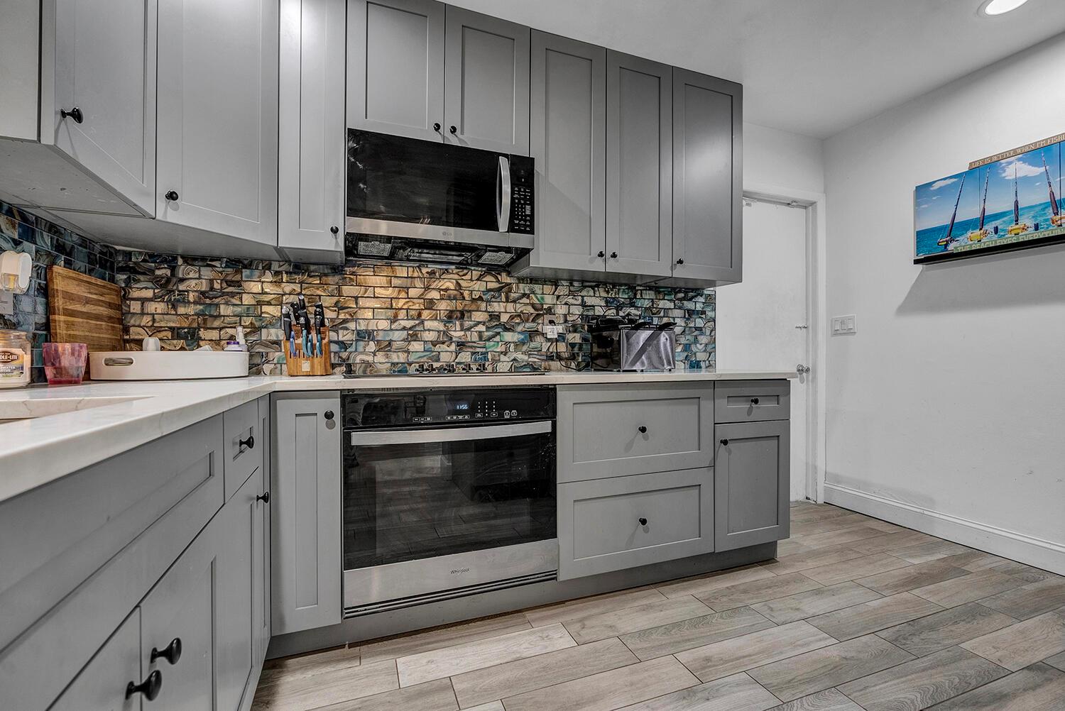 A kitchen features grey cabinets, a patterned tile backsplash, stainless steel appliances, and wood-look flooring — 9544 Richmond Circle, Boca Raton FL 33434, BOCA RATON, FL