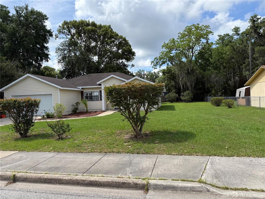 A single-story house with light-colored siding and a large front yard under a cloudy sky — 821 NW 7TH AVENUE, GAINESVILLE, FL