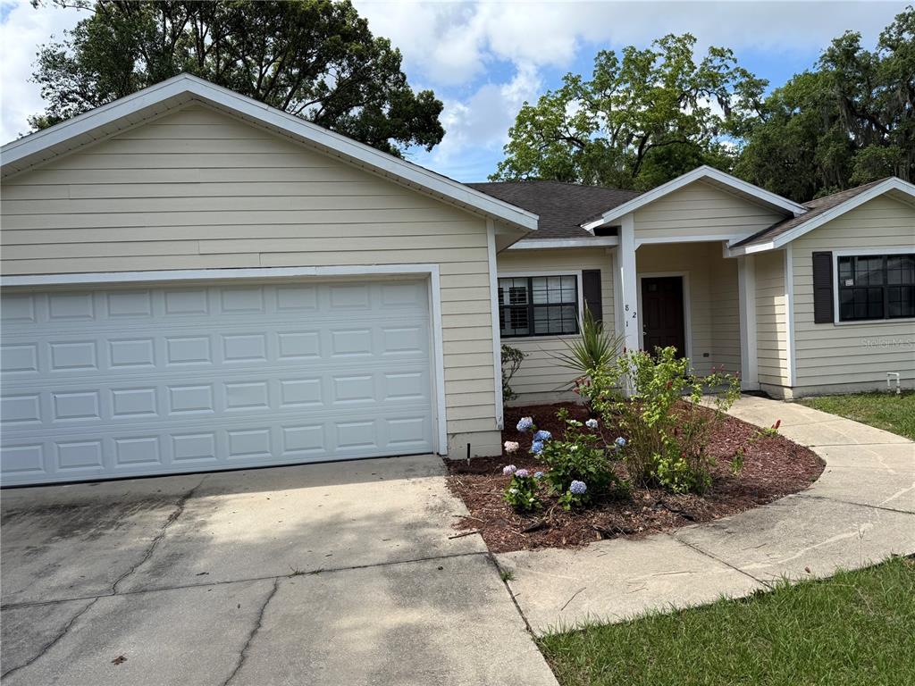 A single-story house with light yellow siding, a two-car garage, and a front garden — 821 NW 7TH AVENUE, GAINESVILLE, FL
