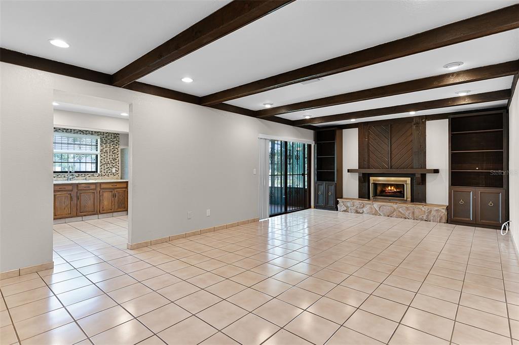 A living room with tile floors, a stone fireplace, built-in shelving, and exposed ceiling beams — 8208 LA SERENA DRIVE, TAMPA, FL