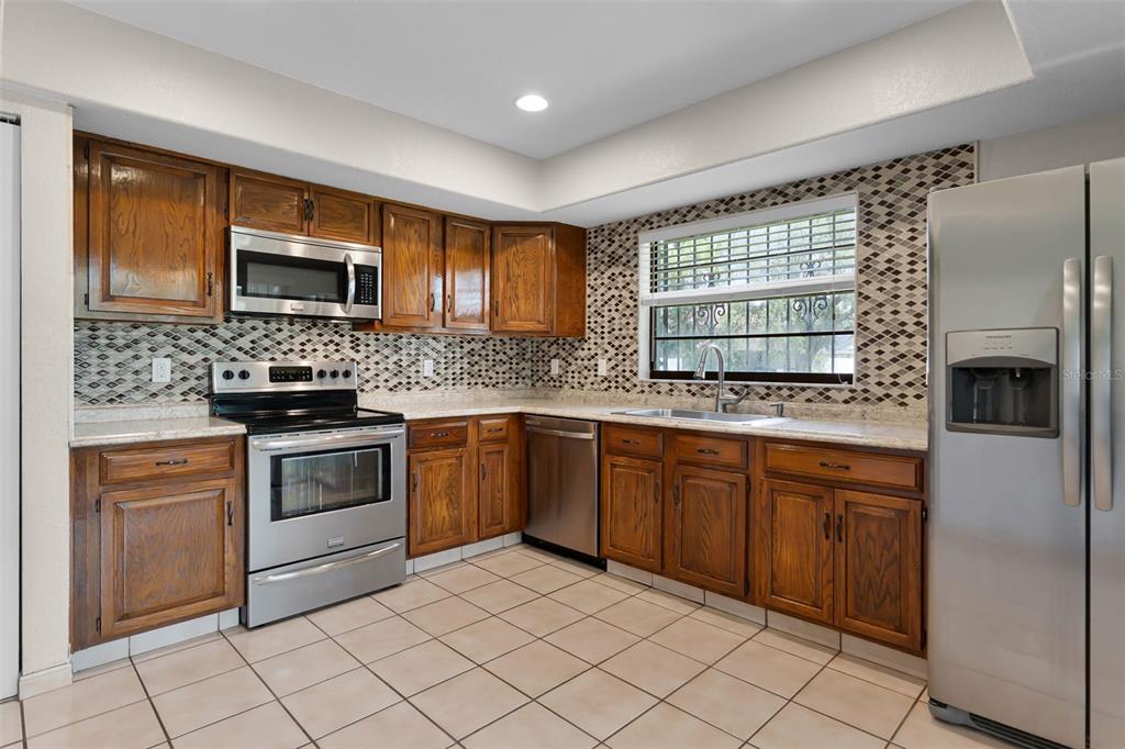 A kitchen with wood cabinets, stainless steel appliances, a patterned tile backsplash, and tiled floors — 8208 LA SERENA DRIVE, TAMPA, FL