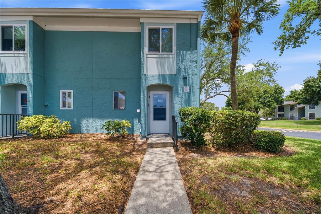 A teal two-story townhouse exterior features a concrete walkway leading to a white front door — 182 115TH AVENUE N UNIT 182, ST PETERSBURG, FL