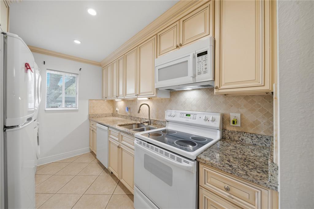 A kitchen features white appliances, granite countertops, beige cabinets, and tile flooring — 182 115TH AVENUE N UNIT 182, ST PETERSBURG, FL
