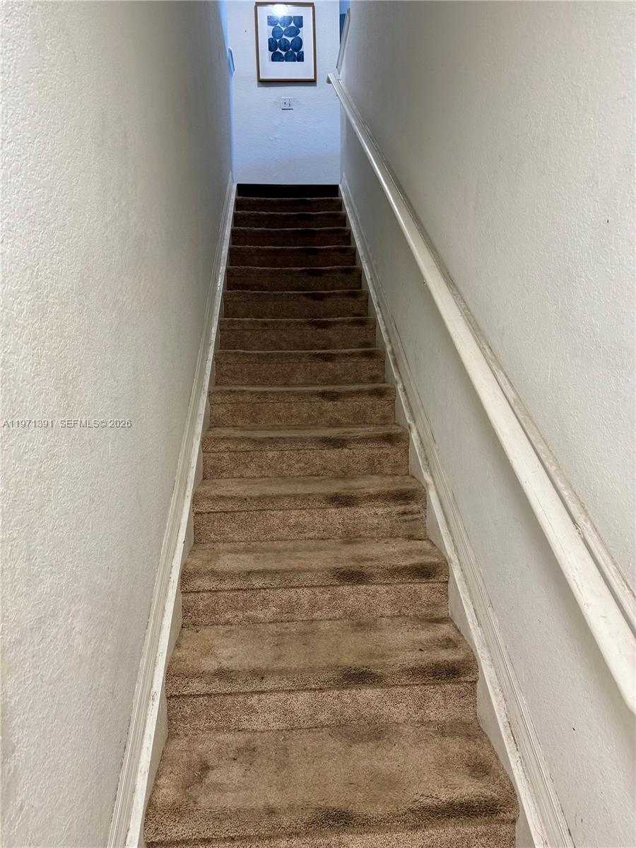 A straight staircase with brown carpeted steps leads upward between two white walls — 2517 Centergate Dr # 203, Miramar FL 33025, MIRAMAR, FL