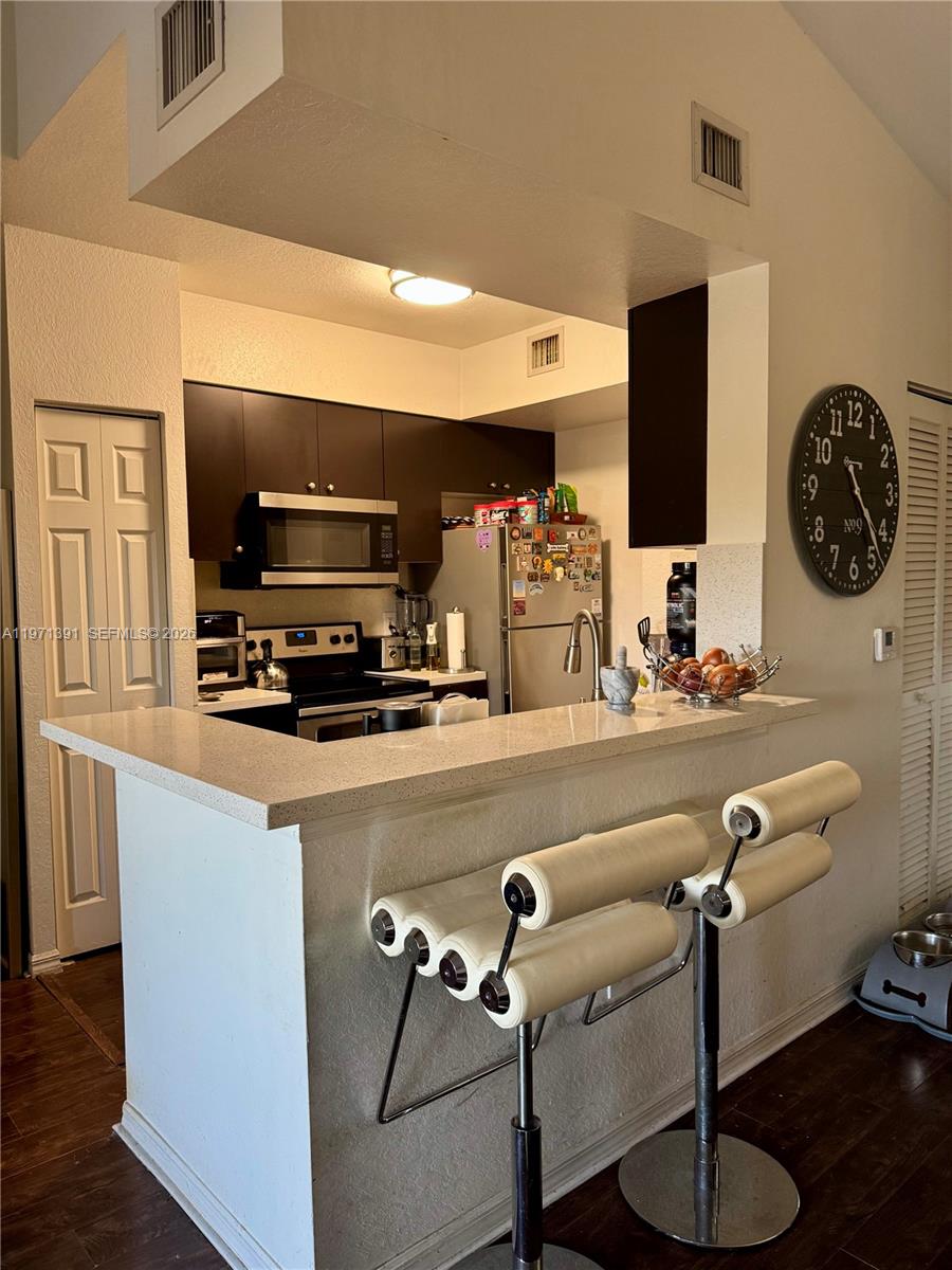 A kitchen features dark cabinets, stainless steel appliances, a breakfast bar, and a wall clock — 2517 Centergate Dr # 203, Miramar FL 33025, MIRAMAR, FL