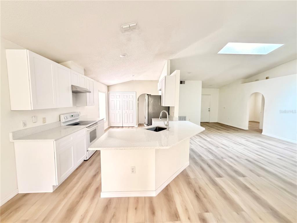 A kitchen with white cabinets, quartz countertops, and light wood-look flooring in an open space — 426 WOODBURY PINES CIRCLE, ORLANDO, FL