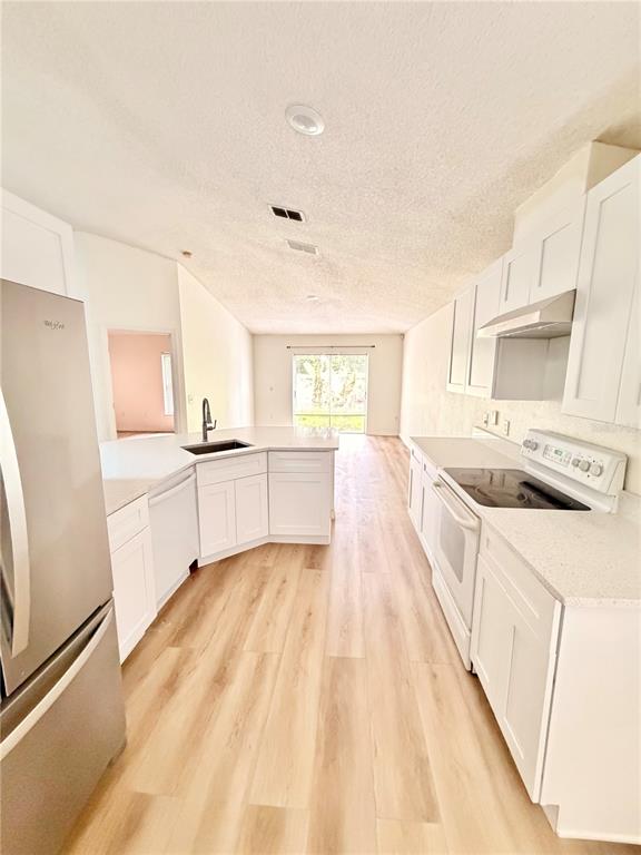 A kitchen features white cabinets, stainless steel appliances, and light wood-look flooring — 426 WOODBURY PINES CIRCLE, ORLANDO, FL