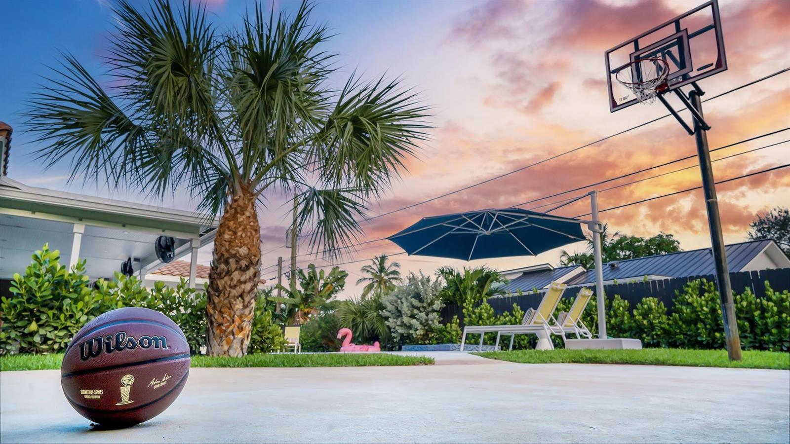 A basketball sits on a concrete patio next to a palm tree and basketball hoop — 518 Sunshine Drive, Delray Beach FL 33444, DELRAY BEACH, FL