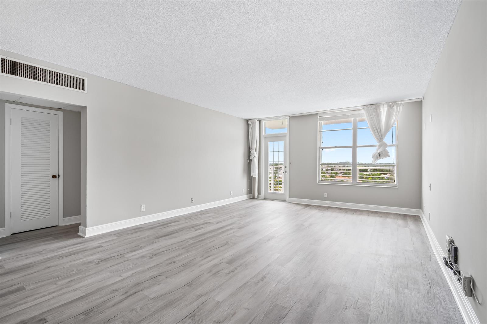 An empty living room features gray wood-look flooring, light gray walls, and a balcony door — 2851 S Ocean # 0026, Boca Raton FL 33432, BOCA RATON, FL