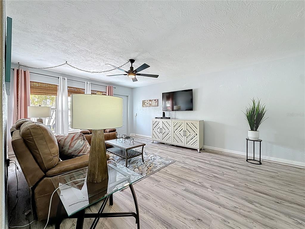 A living room features light gray walls, wood-look flooring, a ceiling fan, and a television — 5861 42ND TERRACE N UNIT 1610, KENNETH CITY, FL