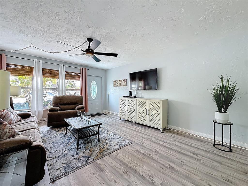 A living room features light gray walls, wood-look flooring, a ceiling fan, and a television — 5861 42ND TERRACE N UNIT 1610, KENNETH CITY, FL
