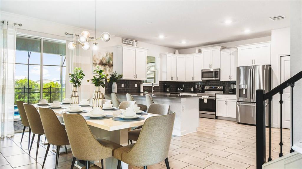 A bright, open-concept kitchen and dining area featuring white cabinetry, stainless appliances, and tile flooring — 2916 SIMILE STREET, KISSIMMEE, FL