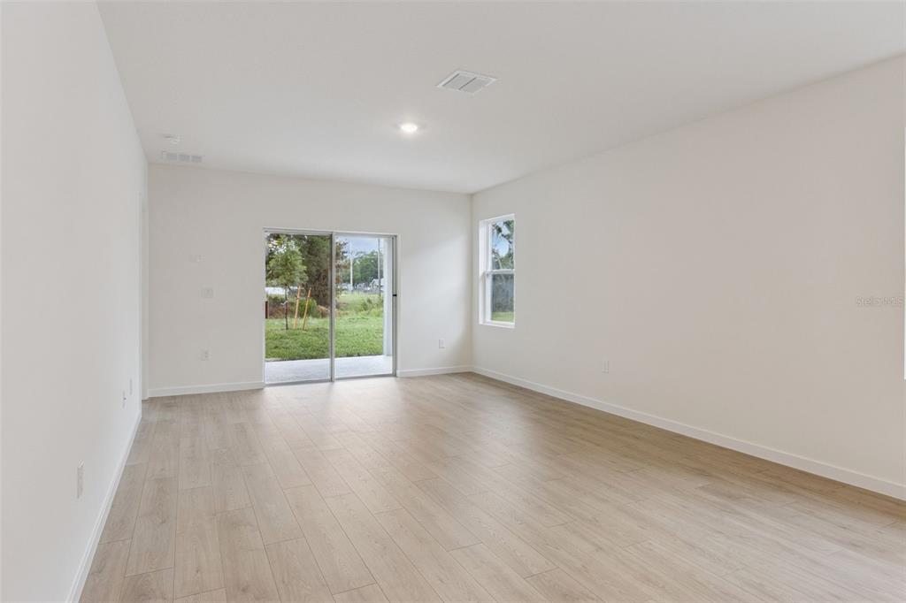 An empty room with light wood-look flooring, white walls, a sliding glass door, and window — 1364 GRAND FLORA LANE, SANFORD, FL
