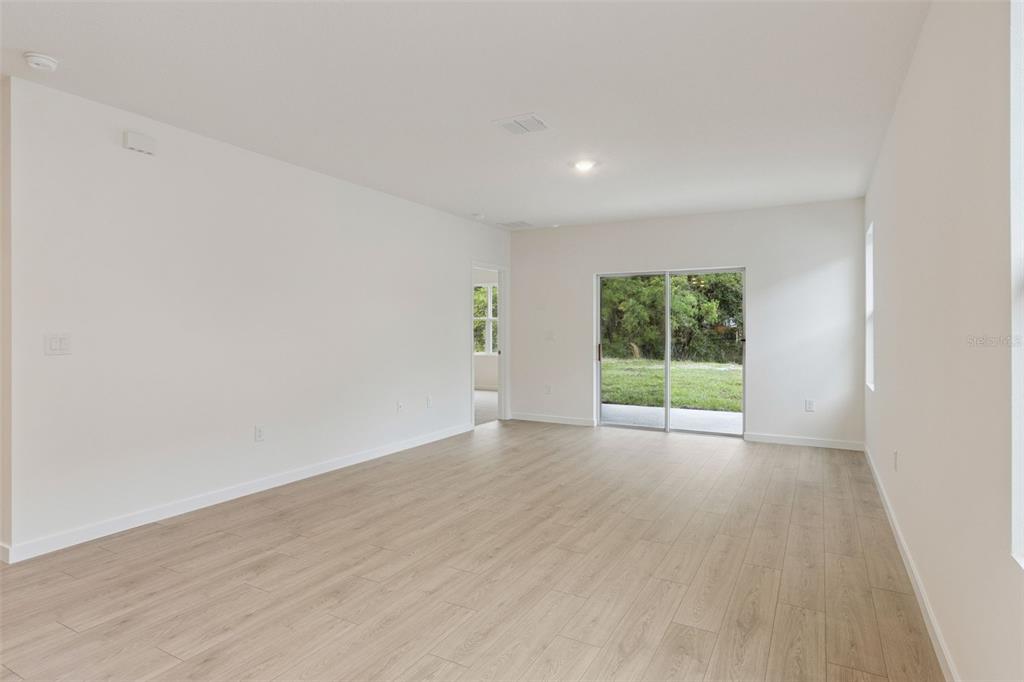 An empty living room features light wood-look flooring, white walls, and a sliding glass door — 1364 GRAND FLORA LANE, SANFORD, FL