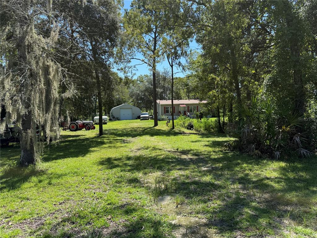 A house and a metal garage sit on a grassy lot surrounded by trees — 6555 SW 165TH COURT, OCALA, FL