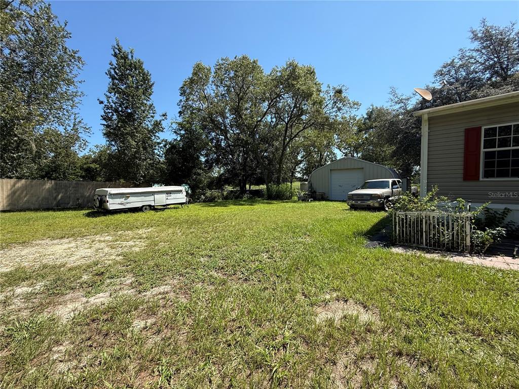 A grassy backyard features a pop-up camper, a detached metal garage, and a pickup truck — 6555 SW 165TH COURT, OCALA, FL