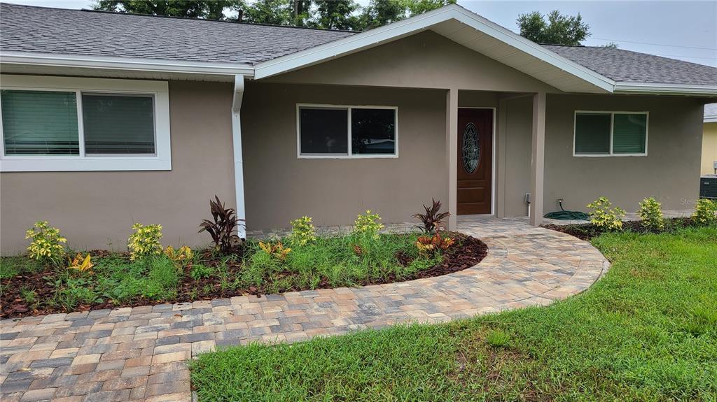 A single-story house exterior features a paver walkway leading to a brown front door — 1718 CARDINAL DR, CLEARWATER, FL