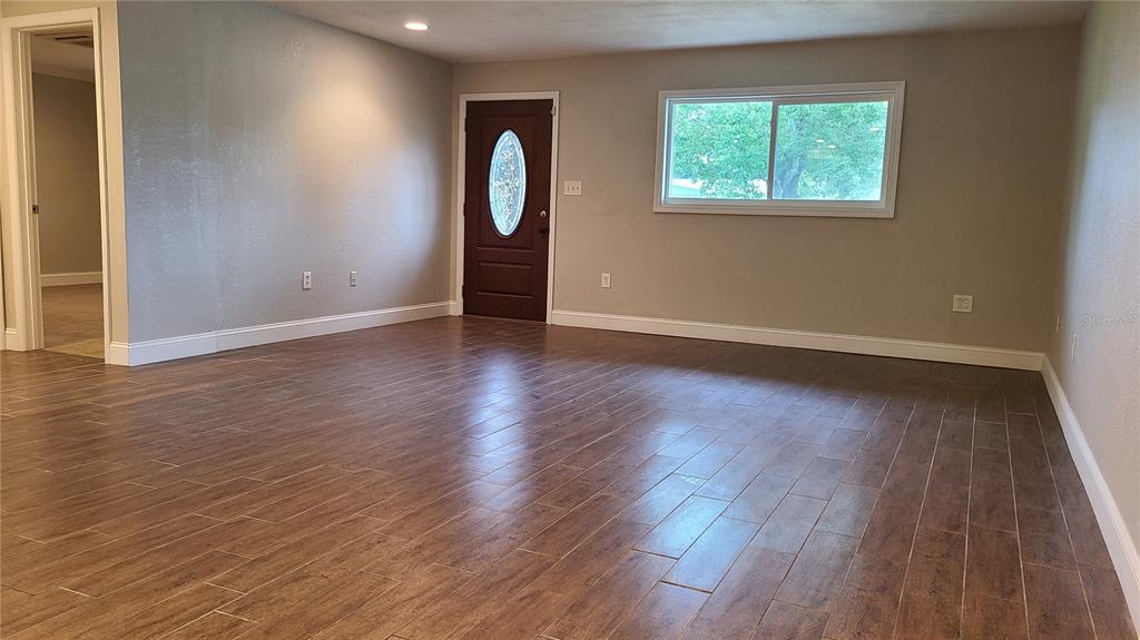 A living room with wood-look tile flooring, a dark brown front door, and a window — 1718 CARDINAL DR, CLEARWATER, FL