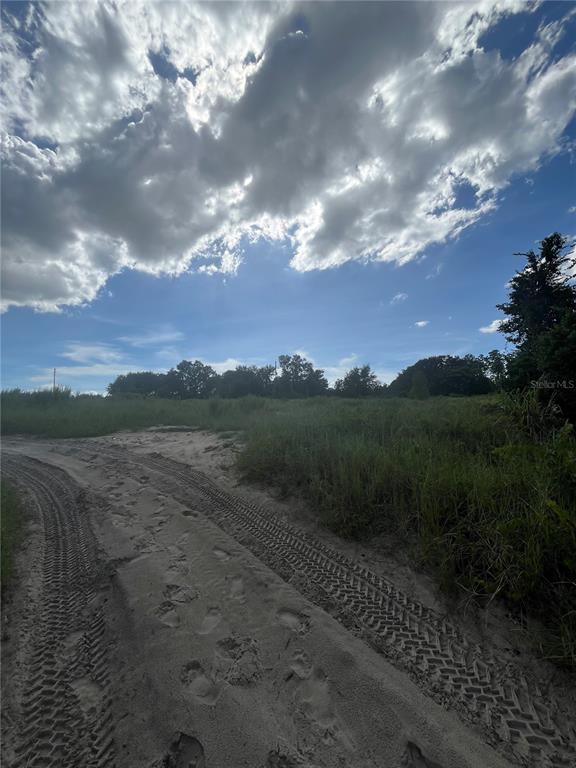 A sandy dirt path leads through a grassy, undeveloped lot under a cloudy blue sky — W KELLY PARK ROAD, APOPKA, FL
