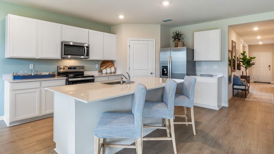 A kitchen features white cabinets, stainless steel appliances, a quartz island, and light wood flooring — 13147 BENDING CREEK TRAIL, PARRISH, FL