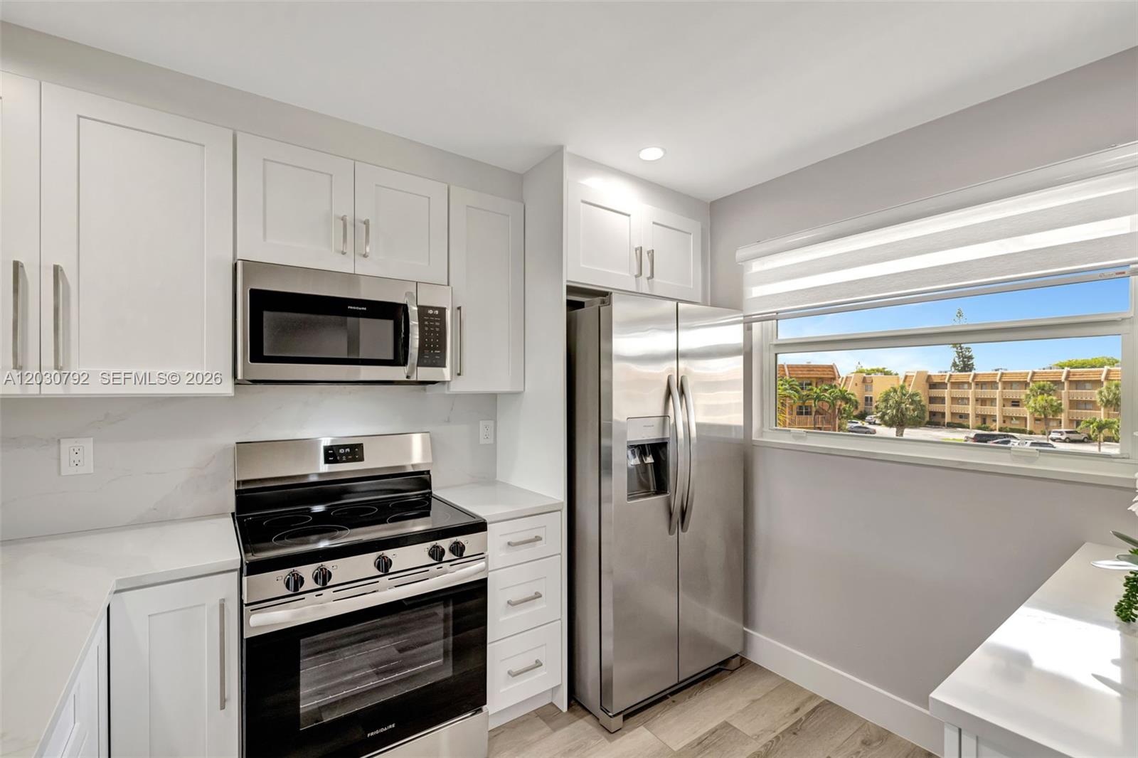 A kitchen features white cabinets, stainless steel appliances, and a window overlooking an apartment complex — 6800 Royal Palm Blvd # 302F, Margate FL 33063, MARGATE, FL