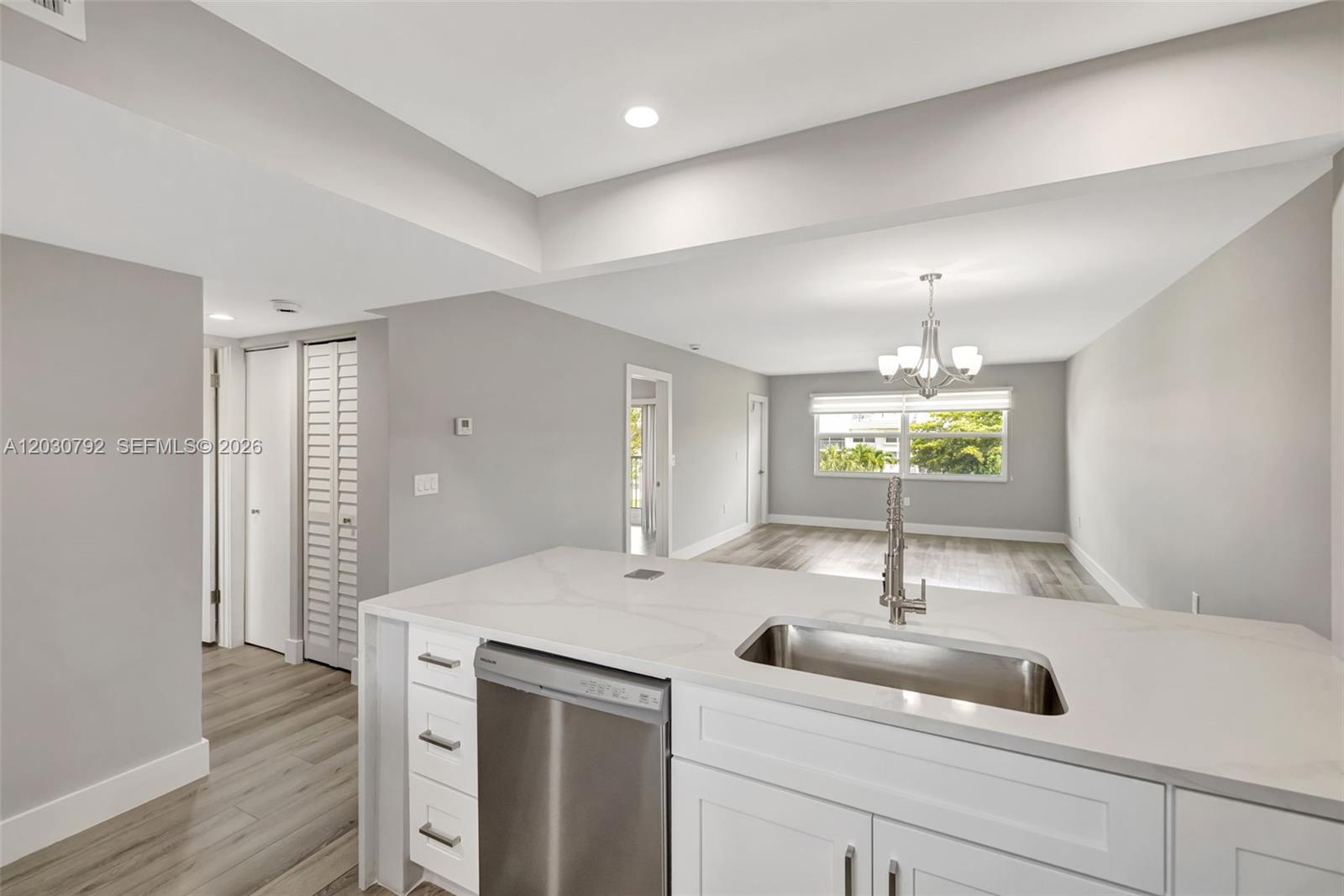 A modern kitchen with white cabinets and quartz countertops overlooks an open dining area — 6800 Royal Palm Blvd # 302F, Margate FL 33063, MARGATE, FL