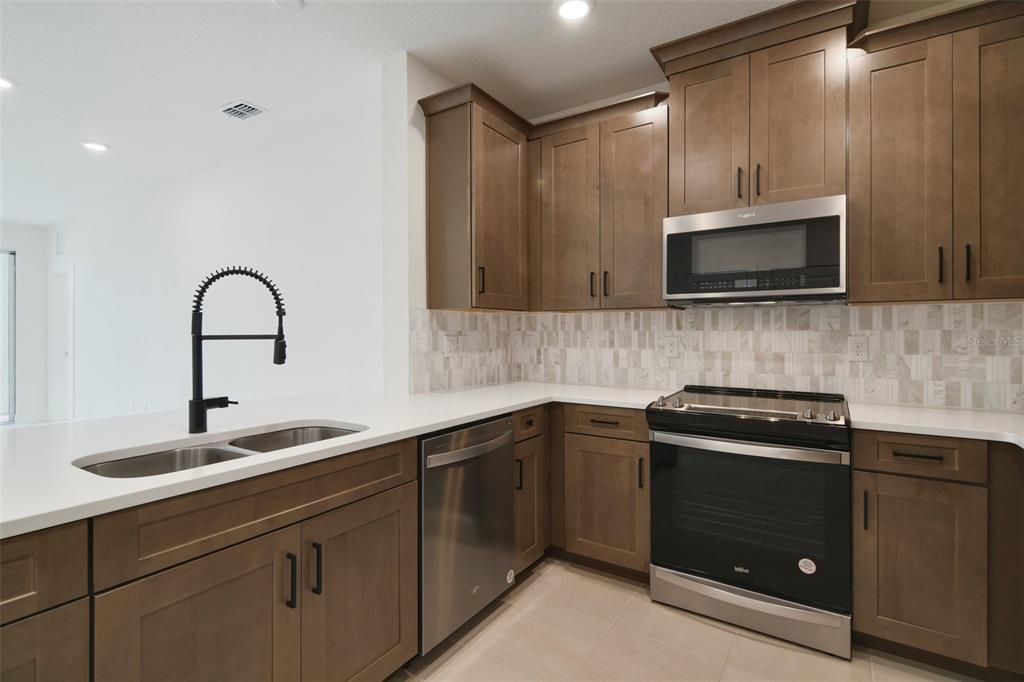 A kitchen with brown cabinets, stainless steel appliances, white countertops, and a tile backsplash — 7557 LAUREATE BOULEVARD UNIT 6301, ORLANDO, FL