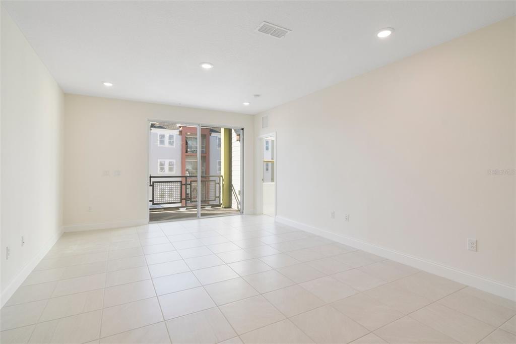 A bright, empty room features white tile flooring, recessed lighting, and a sliding glass door — 7557 LAUREATE BOULEVARD UNIT 6301, ORLANDO, FL