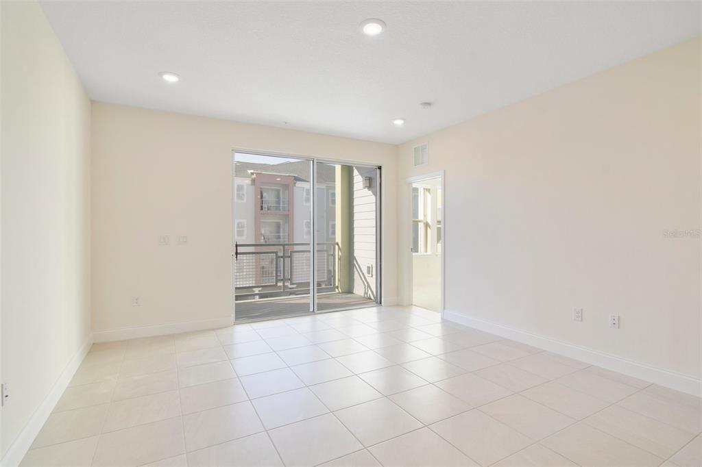 An empty room with light-colored tile flooring, white walls, recessed lighting, and a sliding glass door — 7557 LAUREATE BOULEVARD UNIT 6301, ORLANDO, FL