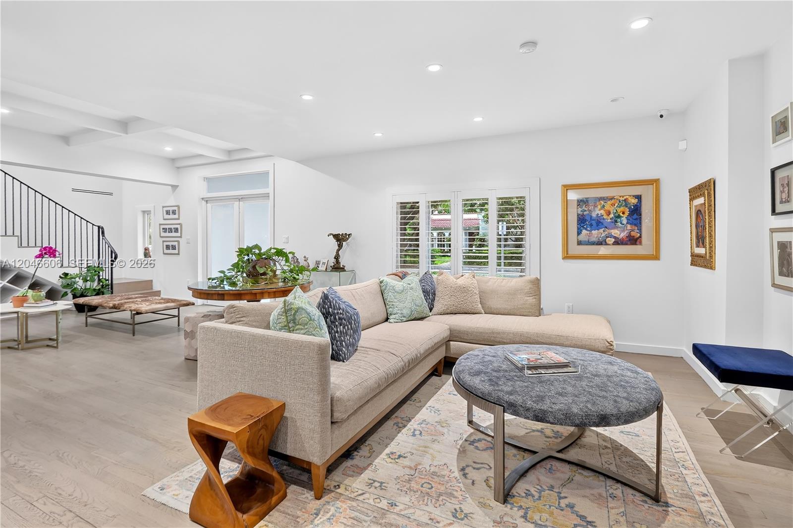 A bright living room features a beige sectional sofa, a round ottoman, and hardwood floors — 100 Sarto Ave., Coral Gables FL 33134, CORAL GABLES, FL